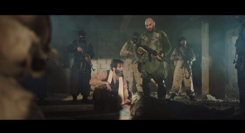 Abu Talha (left, portrayed by Mohammed Al Ahmad), the amīr (commander) of the ISIS fighters, executes a wounded man for crying out for medical treatment. “Who came here longing for life more than death,” Abu Talha observes to Abu Musʿab (right, portrayed by Shadi Al Safadi).